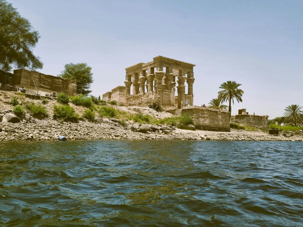 Scenic view of ancient ruins along the Nile River with palm trees and blue sky.